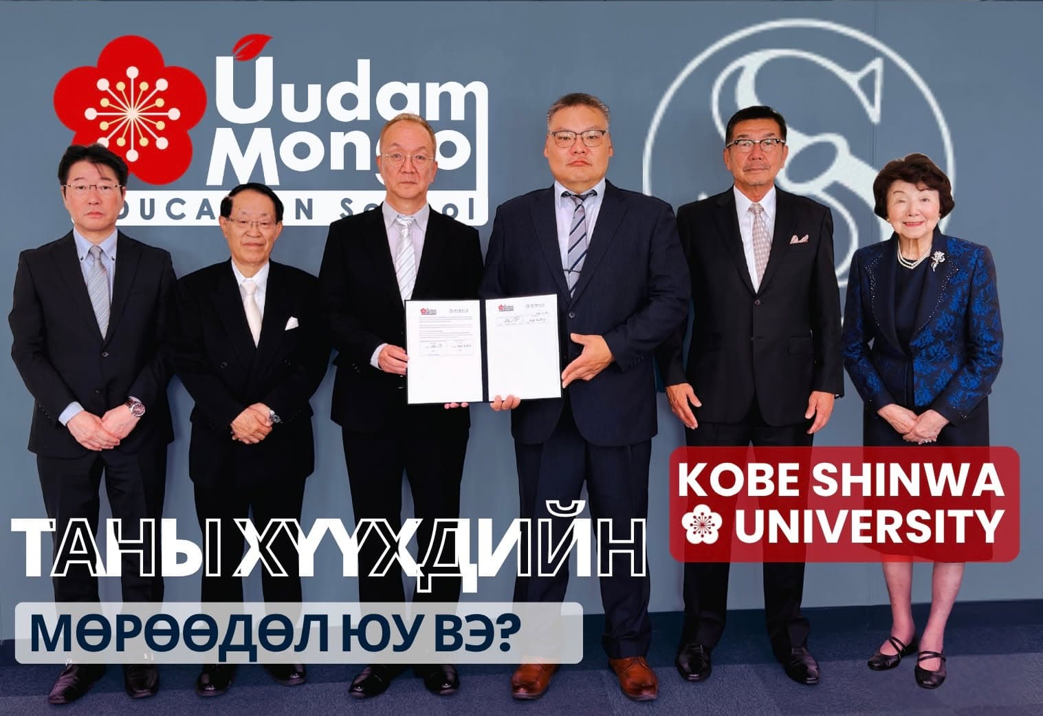 Уудам Монгол сургууль болон Кобэ Шинва их сургуулийн төлөөлөгчид хамтын ажиллагааны гэрээний баримт бичгийг барин, хөх саарал дэвсгэрийн өмнө эгнэн зогссон зураг